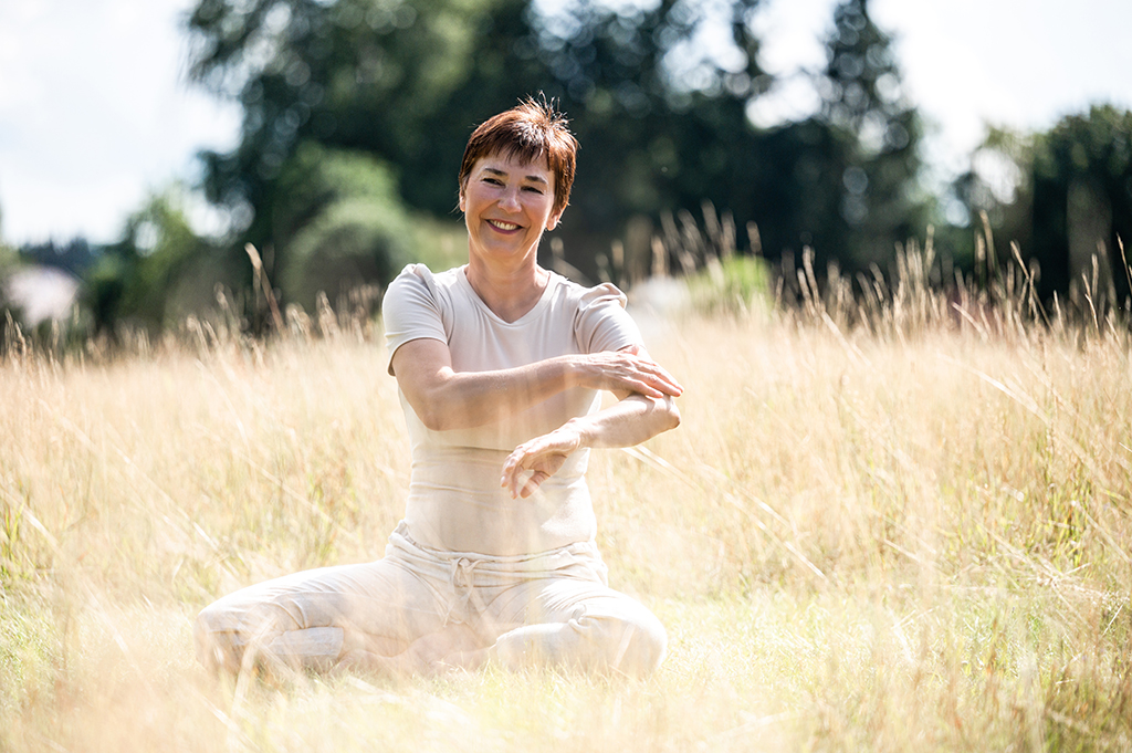 Qigong-Trainerin Ute Gleißner sitzend bei ihren Übungen in einem Kornfeld im Fichtelgebirge